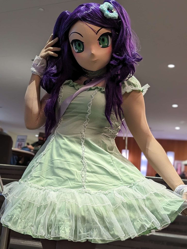 A picture of a kigurumi performer with purple hair and a green lolita style dress.